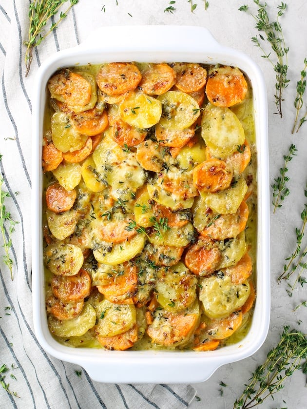 Scalloped Yukon Gold and Sweet Potato Gratin in a white casserole dish surrounded by thyme