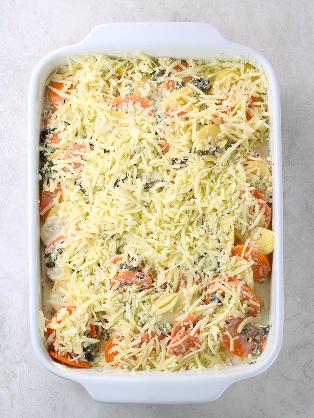 Casserole dish full of sliced yukon gold and sweet potatoes topped Gruyere cheese before cooking