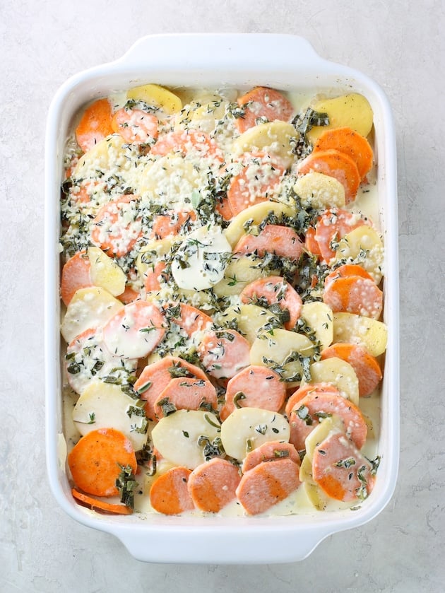 Casserole dish full of sliced yukon gold and sweet potatoes topped with cream sauce before cooking