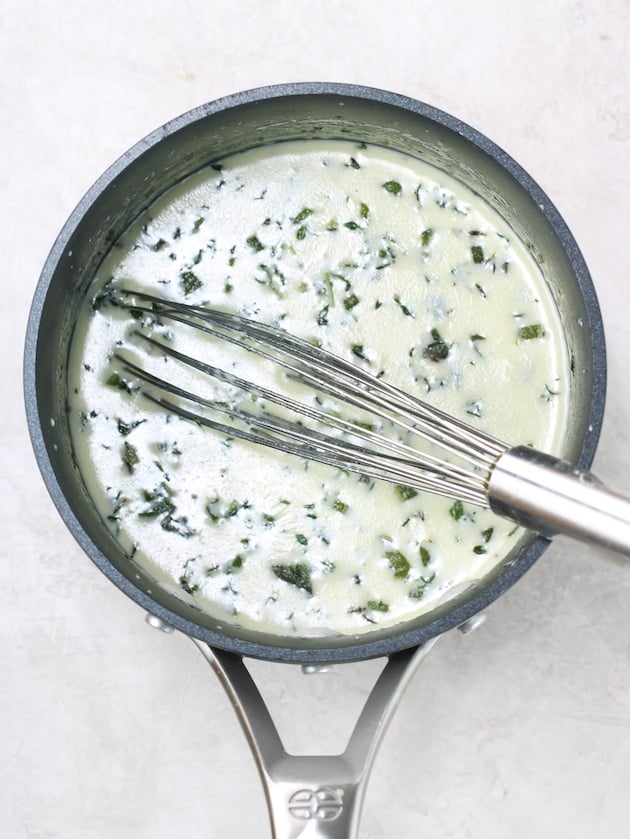 small pot of cream and herbs with wire whisk