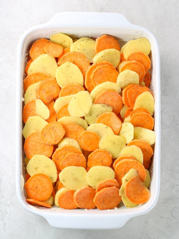 Casserole dish full of sliced yukon gold and sweet potatoes before cooking