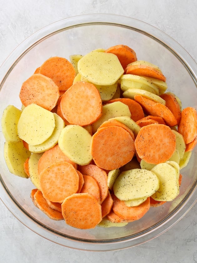 large glass bowl full of sliced sweet potatoes and gold potatoes