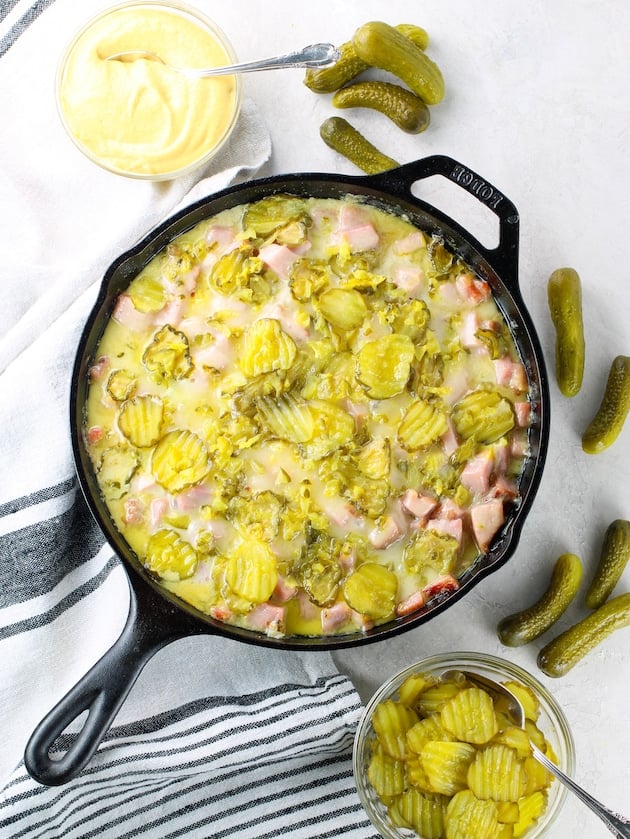 Cast iron skillet of cuban casserole on table with bowls of mustard, pickles
