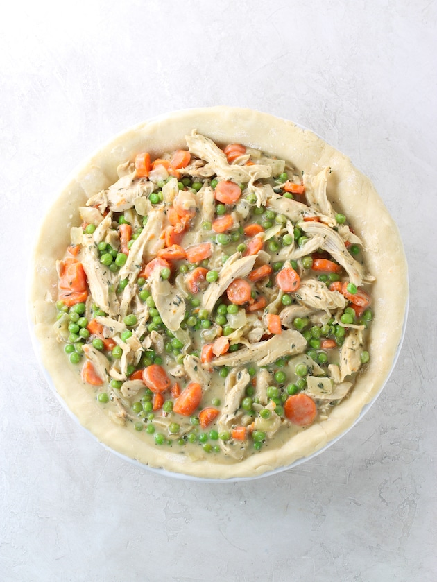 Pie dish with pastry and peas, carrots, chicken before baking