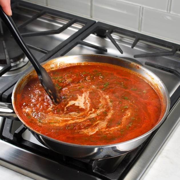 Stirring saute pan of red pasta sauce on stovetop