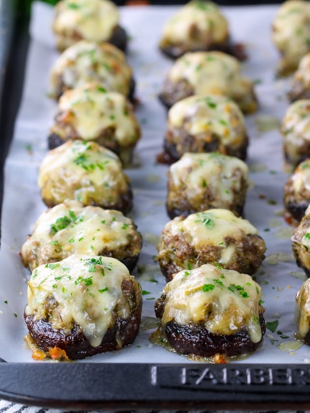 Eye level close up partial baking sheet of stuffed mushrooms topped with melted cheese