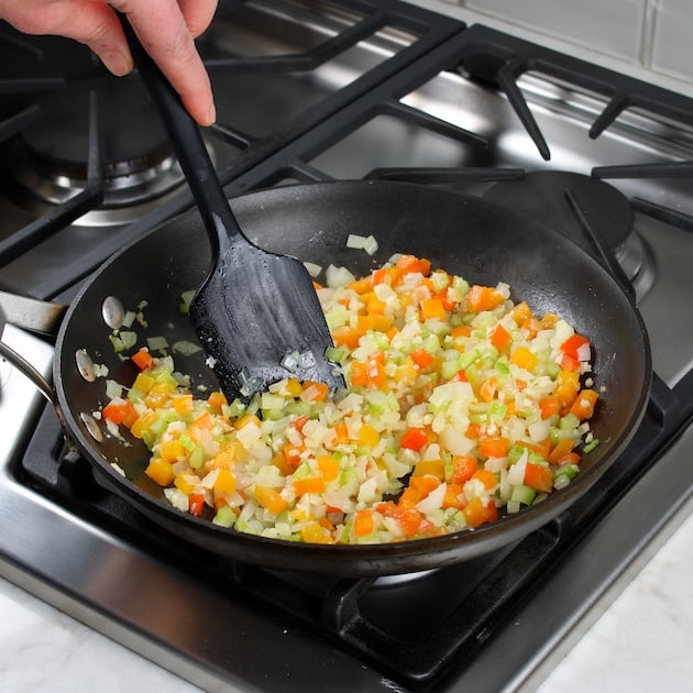 Spatula stirring veggies in saute pan on stovetop