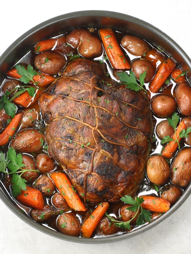 Seared and tied lamb leg in dutch oven with veggies and herbs after roasting