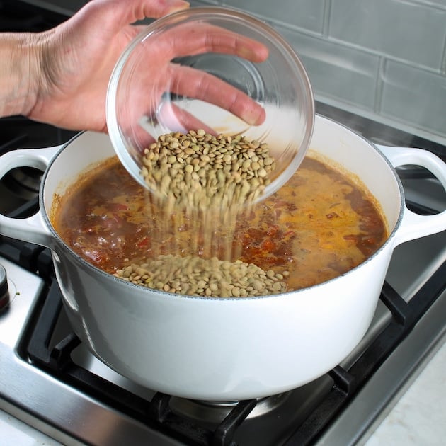 Pouring green lentils into large white soup pot