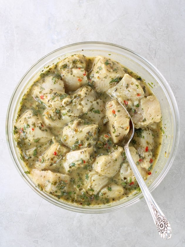 Large glass mixing bowl of chicken in Greek marinade