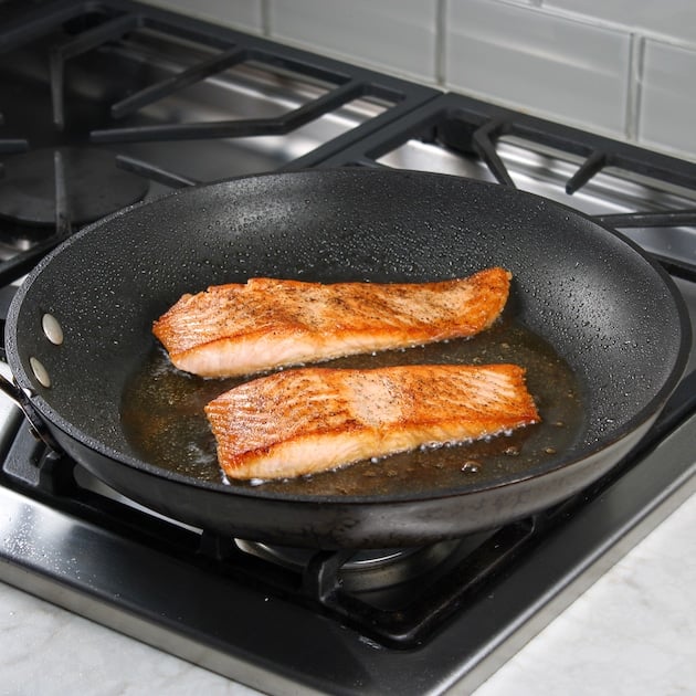 perfectly golden fish filets searing in a saute pan on stovetop