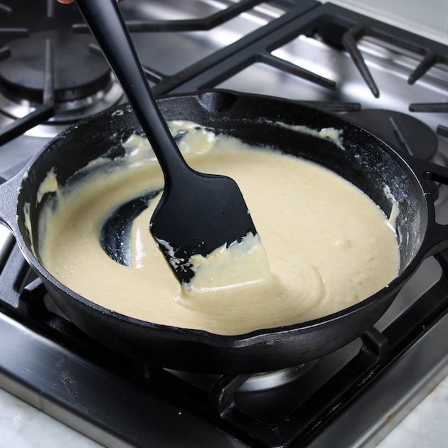 Spatula stirring cheese sauce in cast iron skillet