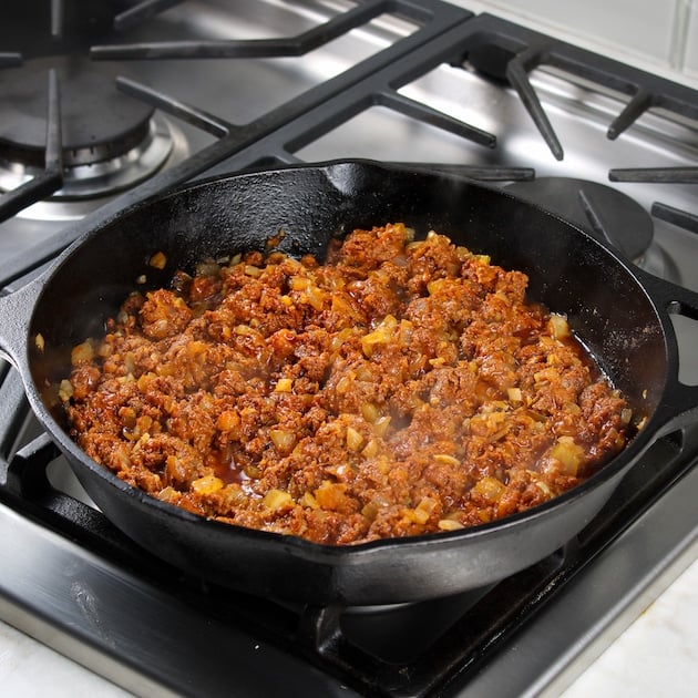 Chorizo cooking in cast iron skillet on the stovetop for choripollo.