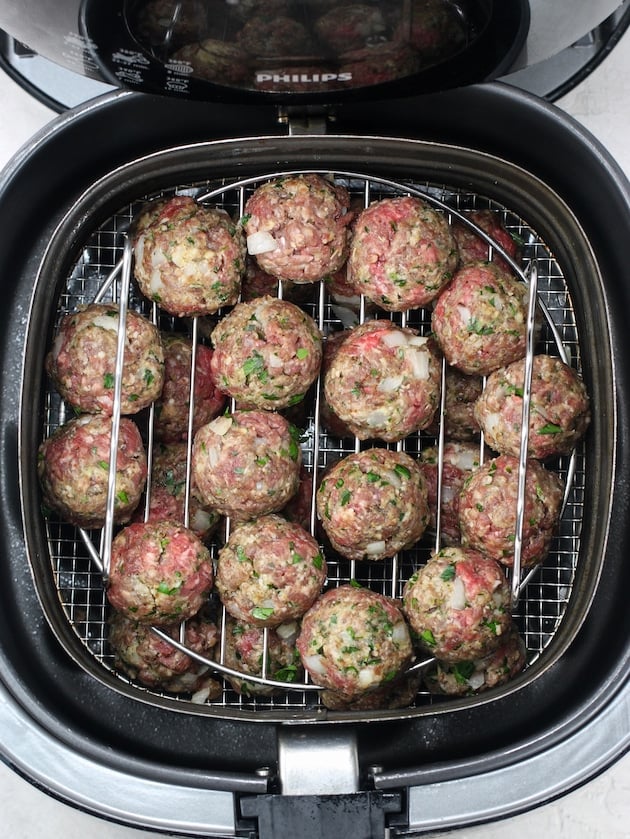 air fryer with meatballs on two baking shelves before cooking