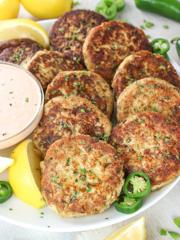 10 Tuna Patties arranged on a plate with Sririacha aioli sauce in a bowl next to them.