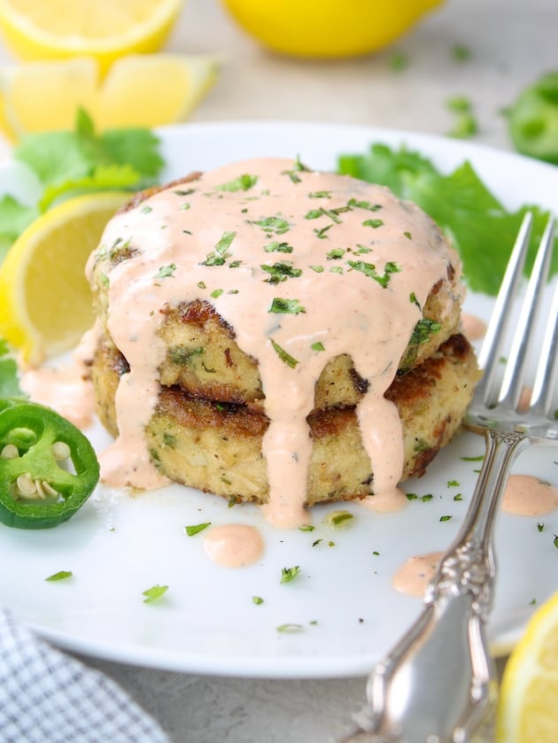 Two Tuna Cakes on a plate with Sriracha aioli drizzled on top of them.