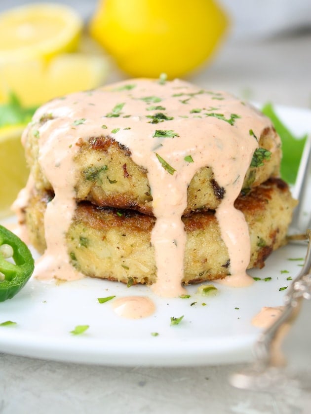 Two Tuna Patties on a plate with a fork and the Sriracha aioli poured on top.