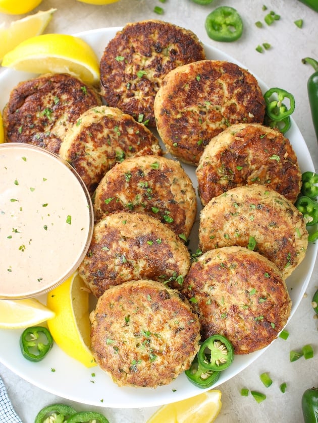 10 Tuna Patties arranged on a plate with Sririacha aioli sauce in a bowl next to them.