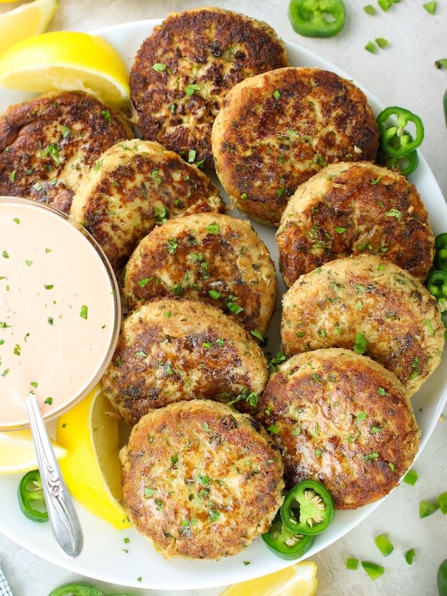 10 Tuna Patties arranged on a plate with Sririacha aioli sauce in a bowl next to them.