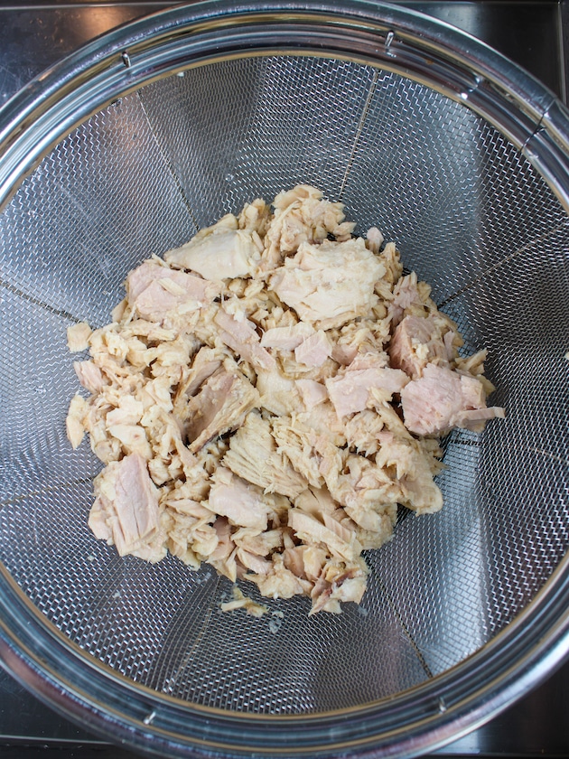 5 cans of 5 ounce solid white canned tuna in a strainer in the sink.