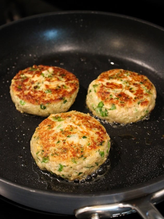 Three Tuna Cakes frying in a nonstick skillet on the stove top.