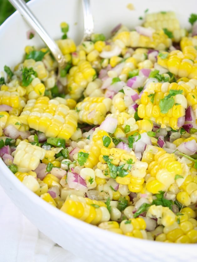 A close up eye level photo of Jalapeño Corn Salad in a serving dish with spoons