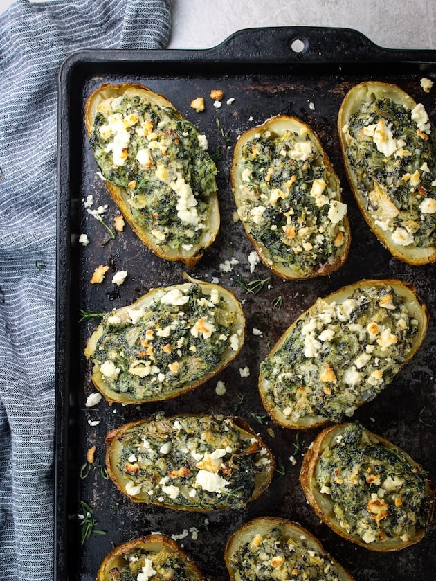 A photo of a baking pan with spinach and artichoke baked potatoes.