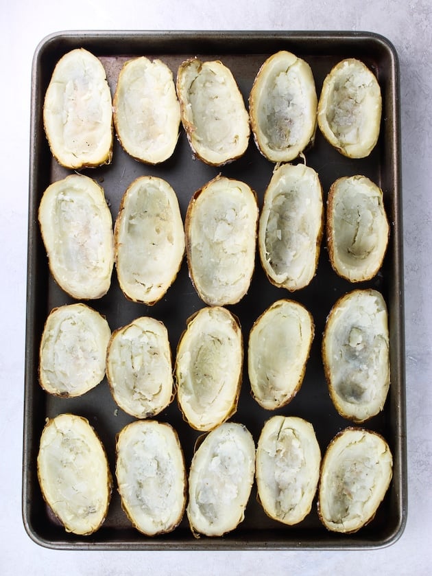 12 baked potatoes cut in have with the potato insides scooped out on a baking sheet.