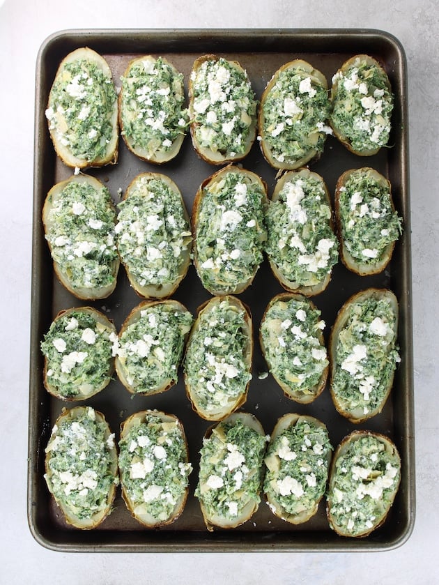 12 baked potatoes cut in half filled with the spinach, artichoke, baked potato mixture on a baking sheet ready to be baked.