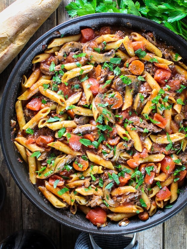 A partial show of Crock-Pot Beef Ragu with Penne in a skillet with bread and wine