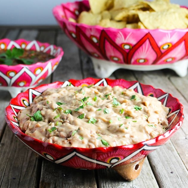 A bowl of creamy cooked Mexican pinto beans with chips and salsa on the side.