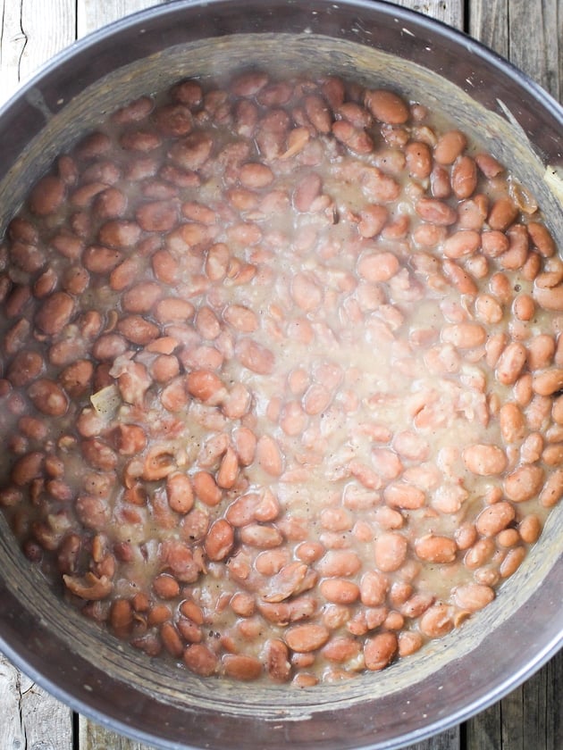 Canned pinto beans cooking in a large pot with chicken stock.