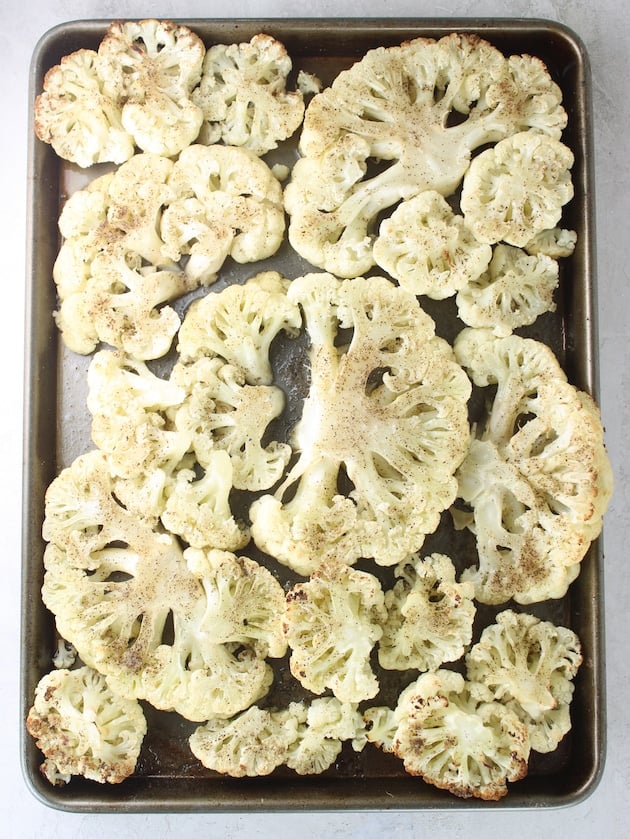Roasted cauliflower on a baking sheet with salt and pepper.