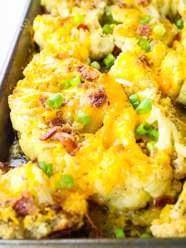A close up photo with roasted Cauliflower steaks topped with cheddar cheese, bacon and green onions.
