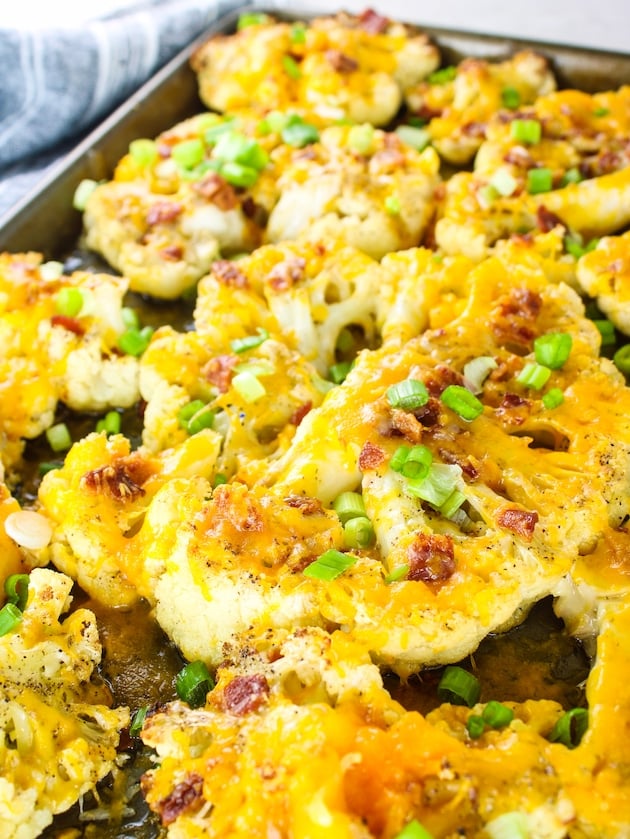 A sheet pan with roasted Cauliflower steaks topped with cheddar cheese, bacon and green onions.