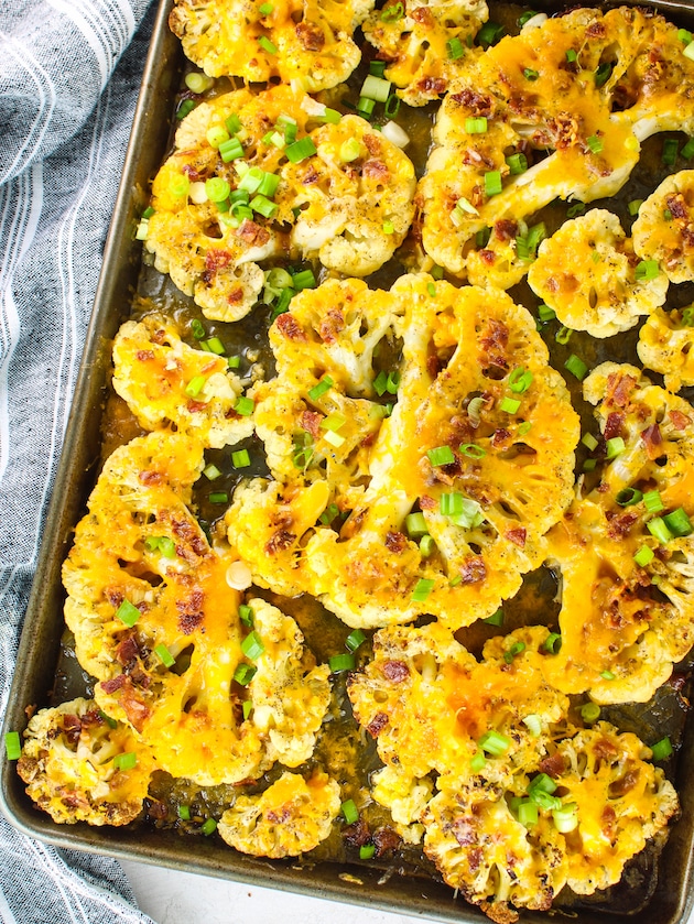 Cauliflower steaks cooked on a baking sheet and topped with cheddar cheese, bacon and green onions.