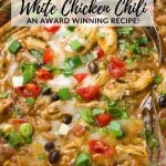 A pot of spicy white chicken chili with toppings like diced tomatoes, chopped cilantro, and green onions.