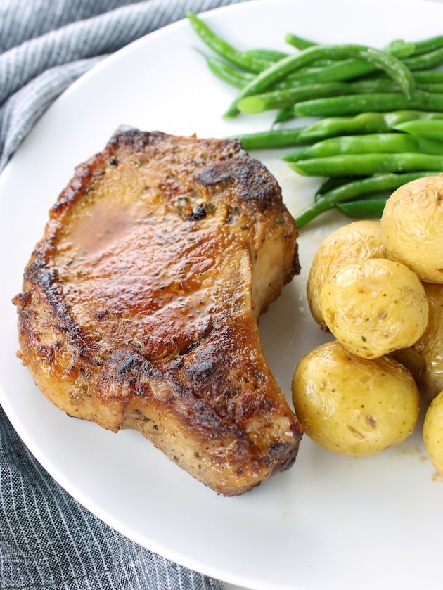 A pork chop on a plate with baby yellow potatoes and green beans.