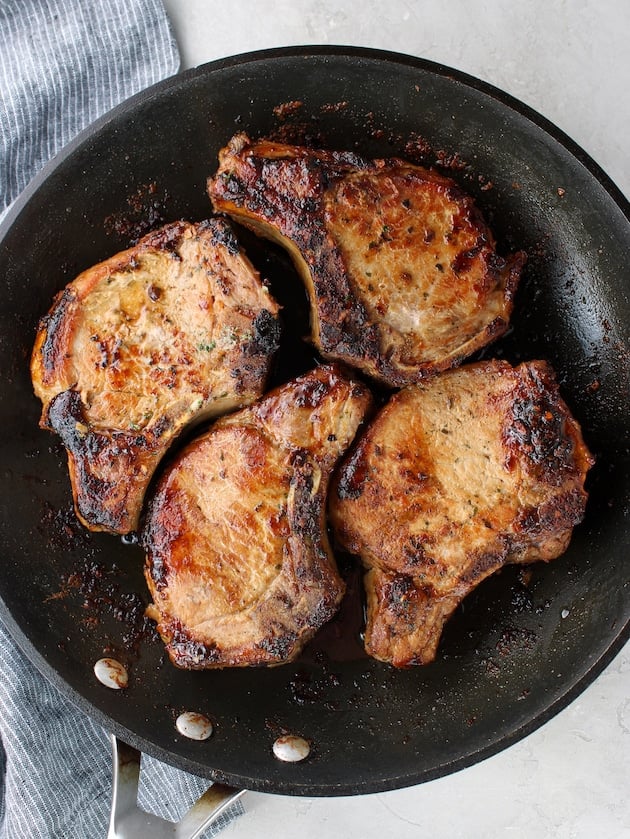 Four pork chops pan-fried in a skillet