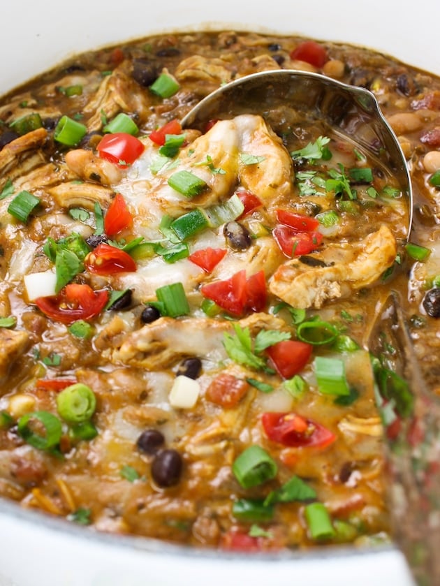 A close up photo of the white chicken chili with cheese, tomatoes and toppings.