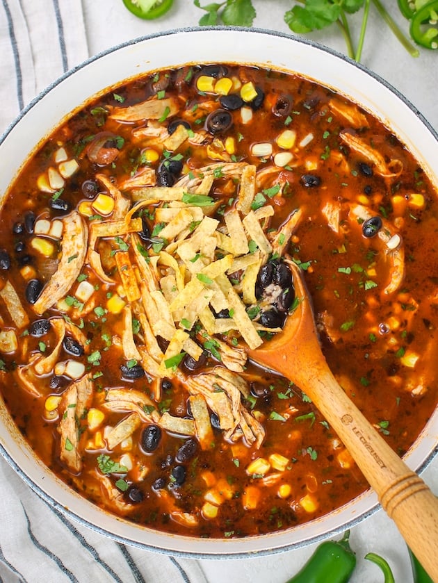 Chicken tortilla soup recipe ready to serve in a large pot with a wooden spoon.