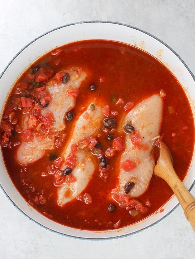 A pot with black beans, tomatoes, chicken broth and raw chicken breasts cooking.