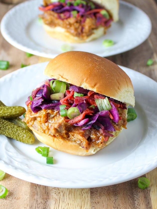 Two plates with pickles and pulled pork sandwhiches.