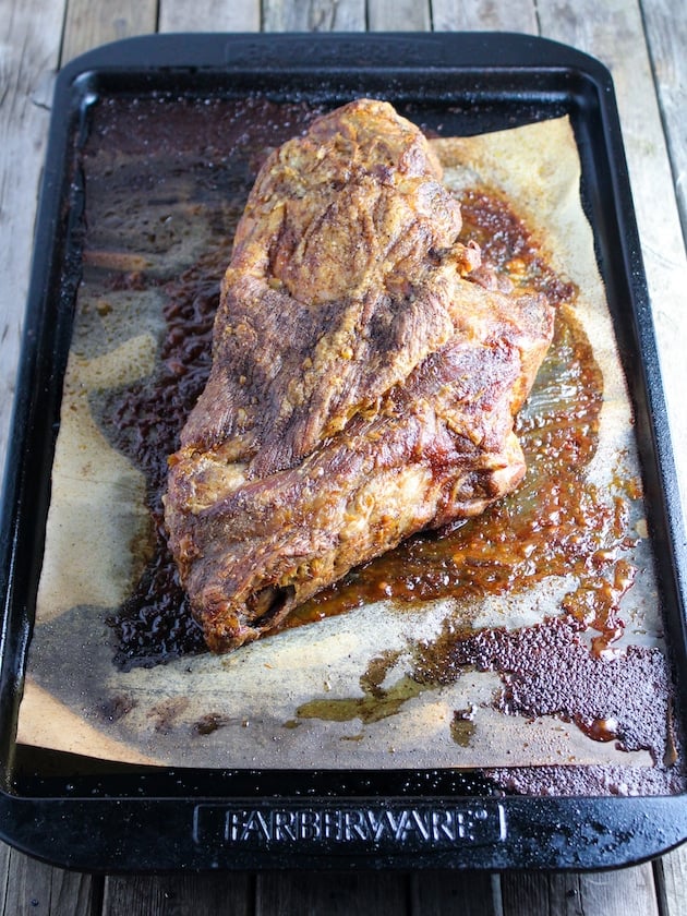 A pork butt slow roasted on a baking sheet with all of it's juices.