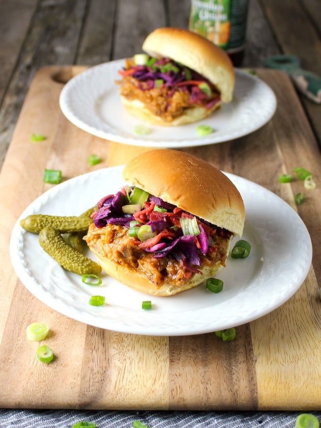 Two plates of BBQ pulled pork sliders with tangy cloeslaw and pickles.