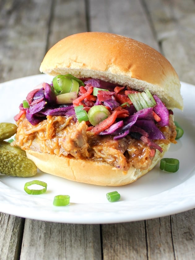 A small plate with a pulled pork sandwich and pickles.