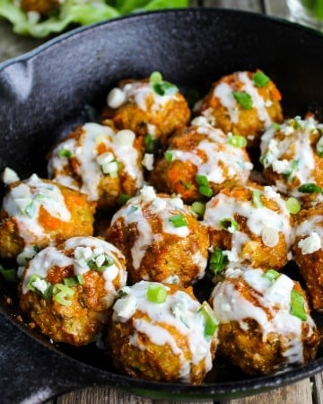 Buffalo chicken meatballs in a cast iron skillet, drizzled with a blue cheese sauce.