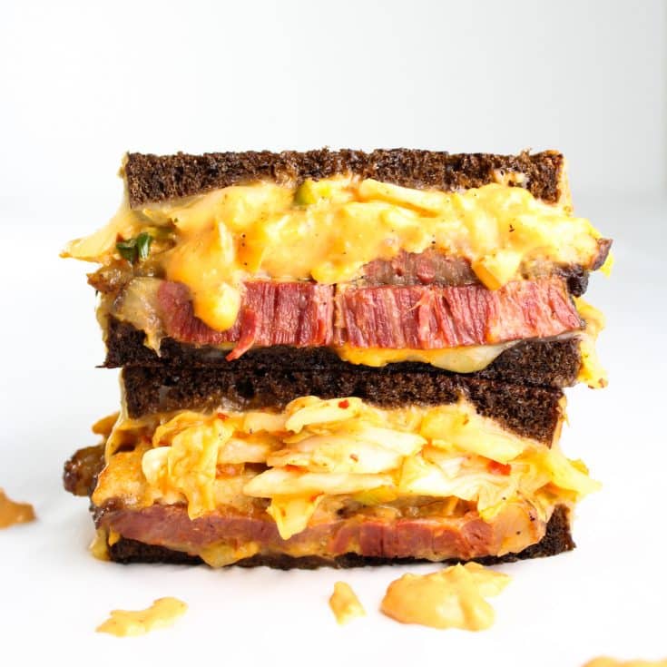 A sandwich with grilled pumpernickel bread, layered with tender corned beef, Swiss cheese, and kimchi, and loaded with homemade tangy Russian dressing.