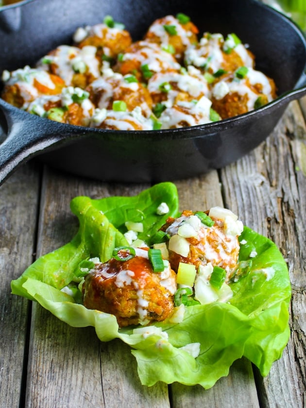 A lettuce wrap with two meatballs and a pan in the background with more chicken meatballs. All tossed in buffalo sauce and blue cheese sauce.