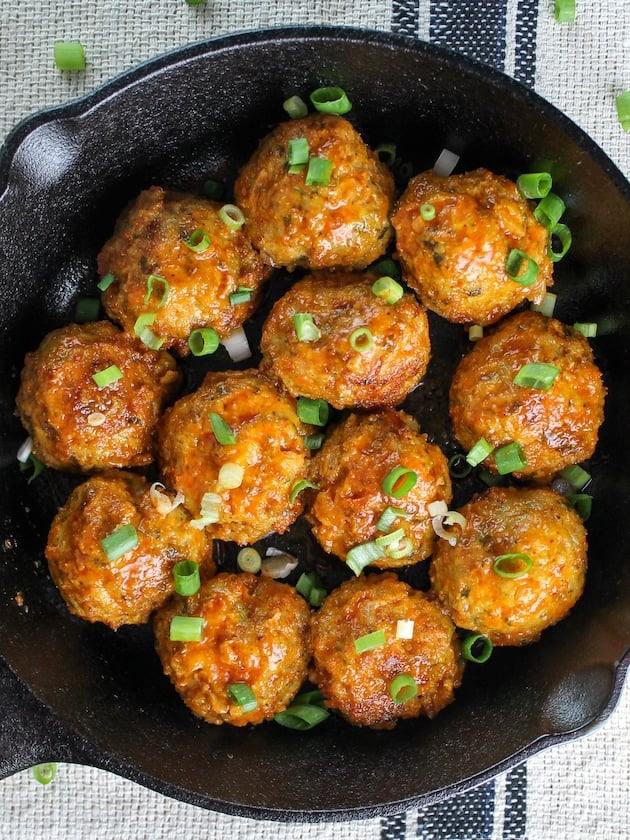Chicken meatballs in a pan tossed with buffalo sauce.